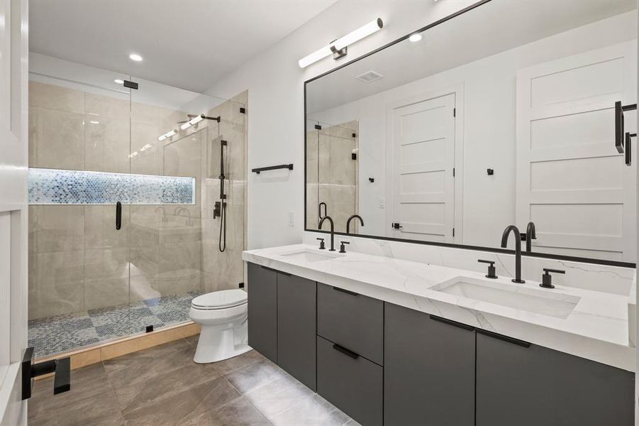 Bathroom with tile patterned flooring, toilet, double vanity, and a shower with shower door