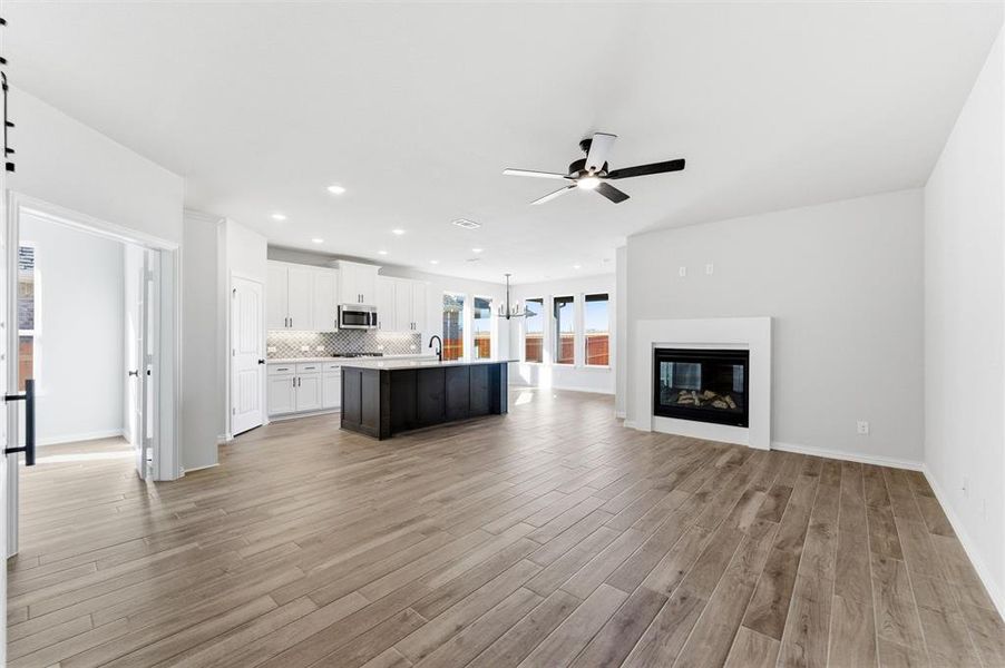 Unfurnished living room featuring light wood-type flooring, a glass covered fireplace, a chandelier, recessed lighting, and ceiling fan