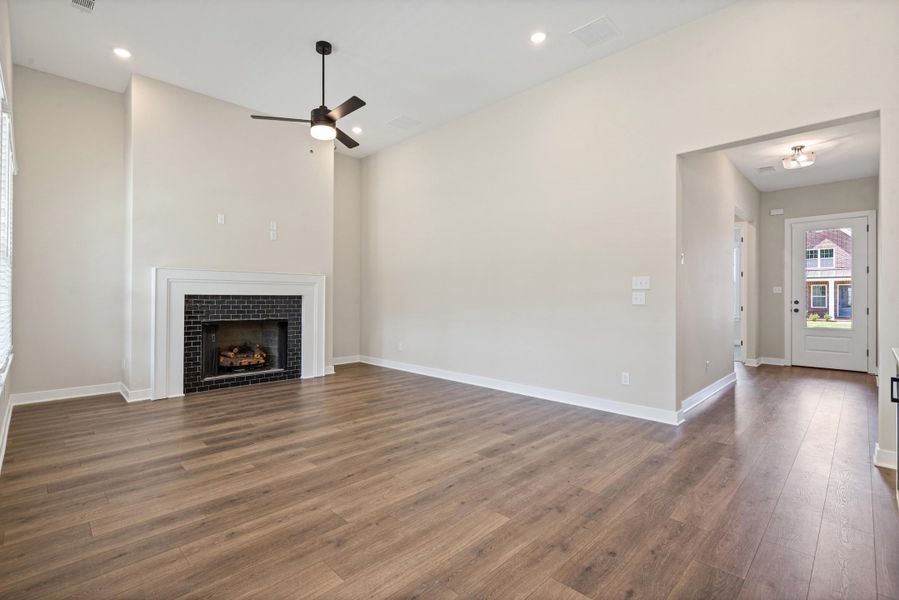 Spacious living area featuring high ceilings, wood-finish flooring, a black brick fireplace with a white mantel, recessed lighting, and a ceiling fan Spacious living area featuring high ceilings, wood-finish flooring, a black brick fireplace with a white mantel, recessed lighting, and a ceiling fan