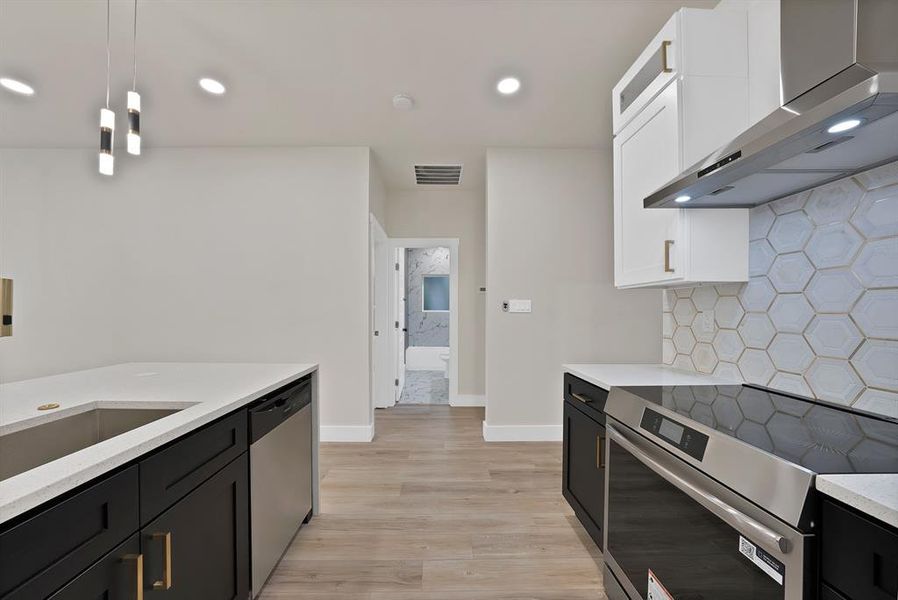 Kitchen with dark cabinets, appliances with stainless steel finishes, wall chimney exhaust hood, light stone countertops, and white cabinetry