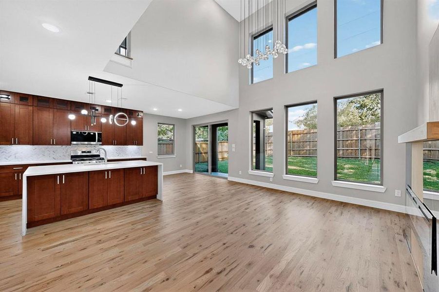 Kitchen featuring pendant lighting, light wood-style flooring, an island with sink, tasteful backsplash, and a high ceiling