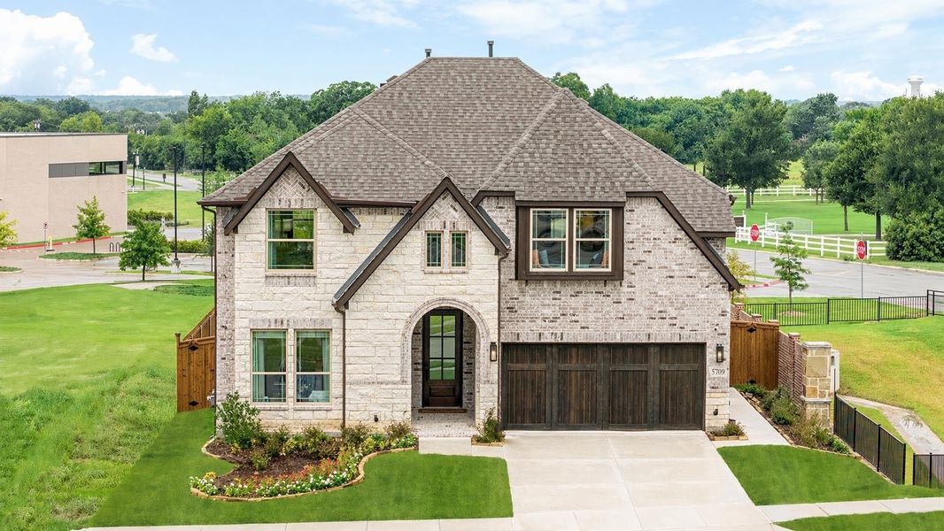 Two-story stone and brick home with arched entry, dark wood garage door, and manicured front lawn Two-story stone and brick home with arched entry, dark wood garage door, and manicured front lawn