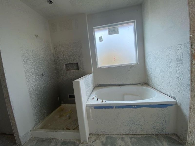 Spacious bathroom under construction, featuring a corner soaking tub with a surrounding half-wall and a window above