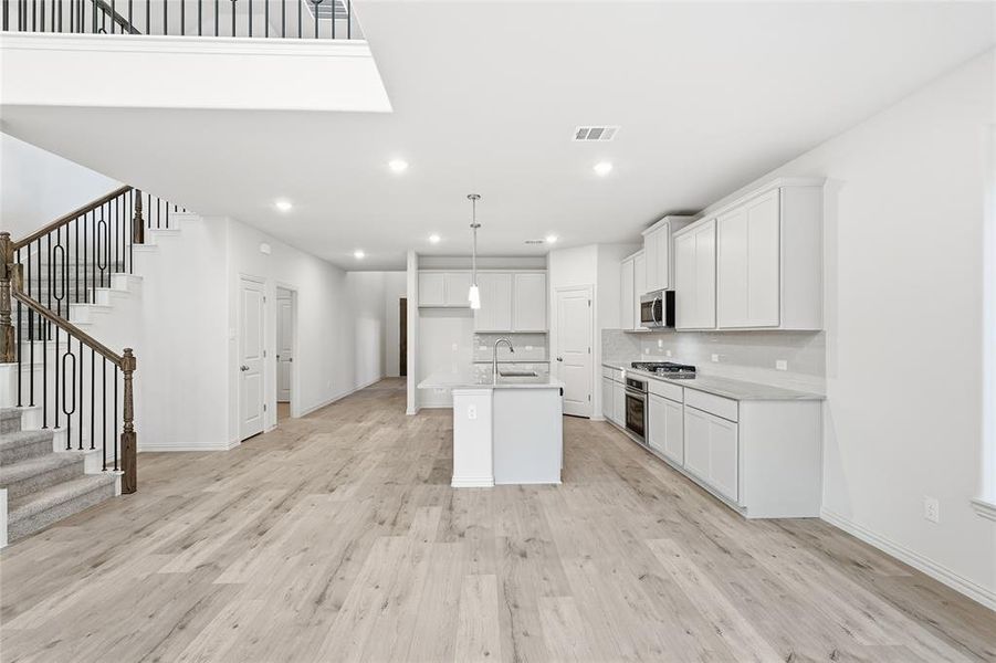 Kitchen with white cabinets, an island with sink, light wood-style flooring, open floor plan, and recessed lighting