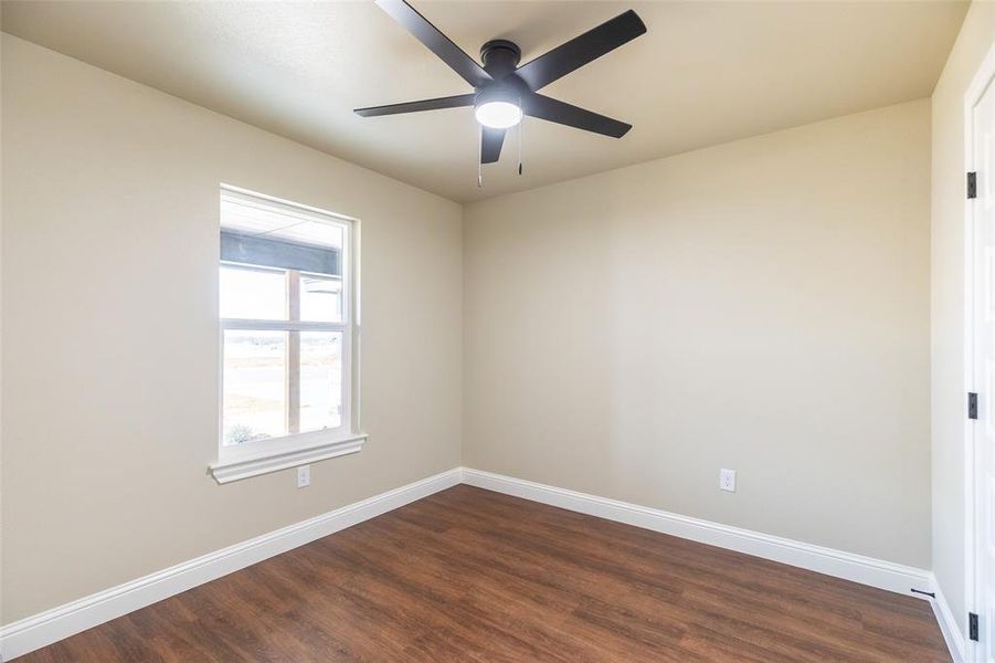 Neutral-toned room featuring a black ceiling fan with integrated lighting, a double-hung window, wood-finish flooring, and white baseboards