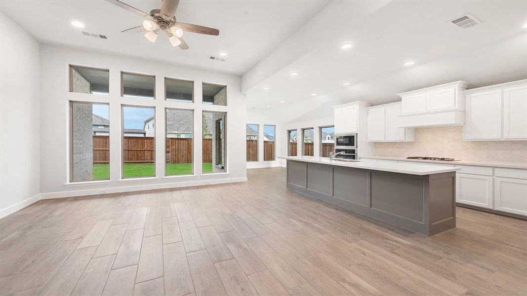 Kitchen with custom exhaust hood, a wealth of natural light, decorative backsplash, and light wood-type flooring