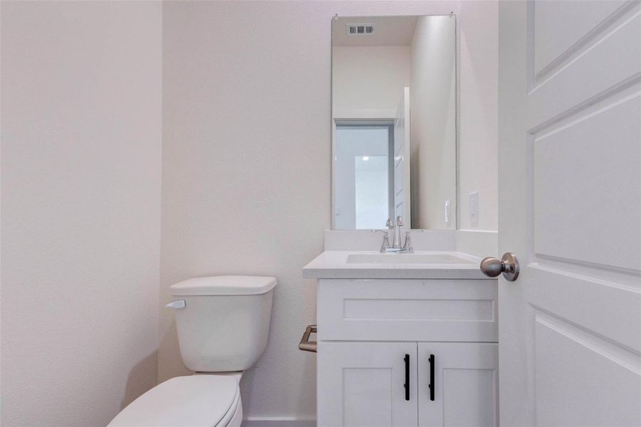 Convenient powder bath featuring a clean white vanity, quartz-style countertop, modern plumbing fixture, framed mirror, and neutral finishes. The compact layout is practical and polished, offering an ideal guest bath on the main level. White cabinetry with black hardware adds a crisp modern contrast while keeping the space bright and fresh. Convenient powder bath featuring a clean white vanity, quartz-style countertop, modern plumbing fixture, framed mirror, and neutral finishes. The compact layout is practical and polished, offering an ideal guest bath on the main level. White cabinetry with black hardware adds a crisp modern contrast while keeping the space bright and fresh.