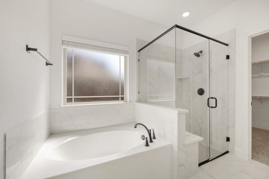 Master bathroom with soaking tub, glass-enclosed shower, marble tile walls, and walk-in closet entry
