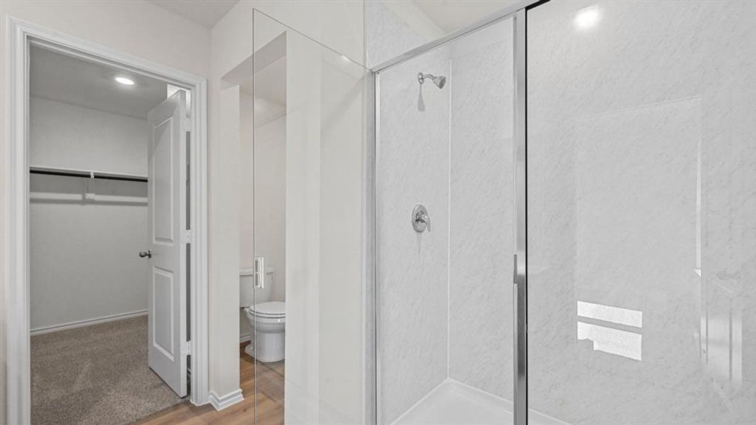 Bathroom featuring a clear glass shower enclosure, white shower surround, chrome fixtures, and a toilet with wood-finish flooring