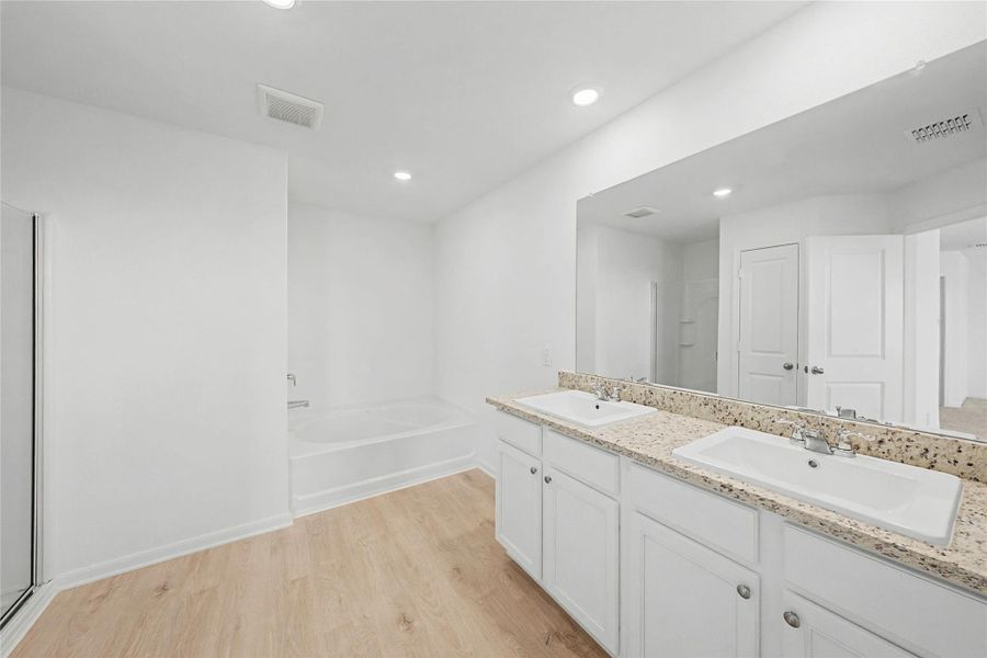 Bathroom featuring light wood-style floors, double vanity, a garden tub, a stall shower, and recessed lighting