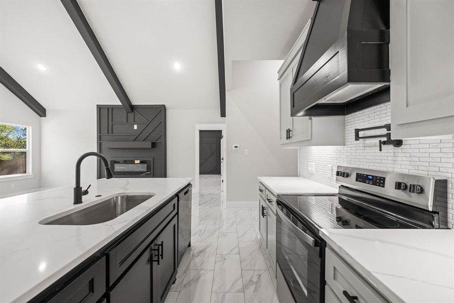 Dual tone kitchen featuring stainless steel electric stove, an island with sink, light stone counters, two tone cabinets, and black dishwasher