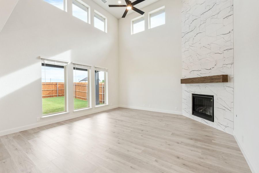 Open living room with high ceilings, stone fireplace, wood mantel, and light hardwood floors Open living room with high ceilings, stone fireplace, wood mantel, and light hardwood floors