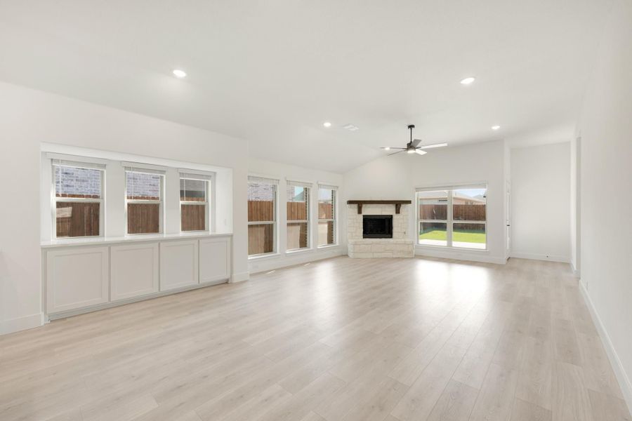 Open living room with light wood floors, stone fireplace, ceiling fan, and large windows Open living room with light wood floors, stone fireplace, ceiling fan, and large windows