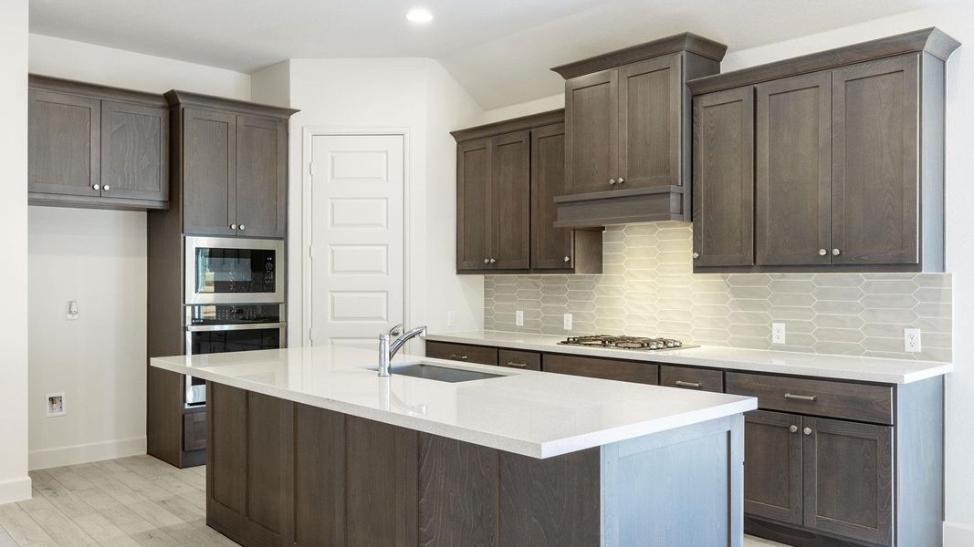 Kitchen with dark brown cabinets, light wood-type flooring, decorative backsplash, stainless steel appliances, and a sink