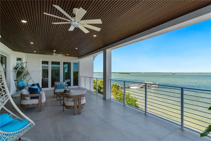 Covered terrace featuring a slatted wood-paneled ceiling, recessed lighting, ceiling fans, large-format tile flooring, and a metal railing system Covered terrace featuring a slatted wood-paneled ceiling, recessed lighting, ceiling fans, large-format tile flooring, and a metal railing system