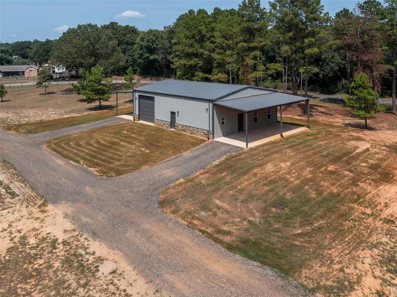 View of front of property with driveway, an outbuilding, a metal roof, covered porch, and a front lawn