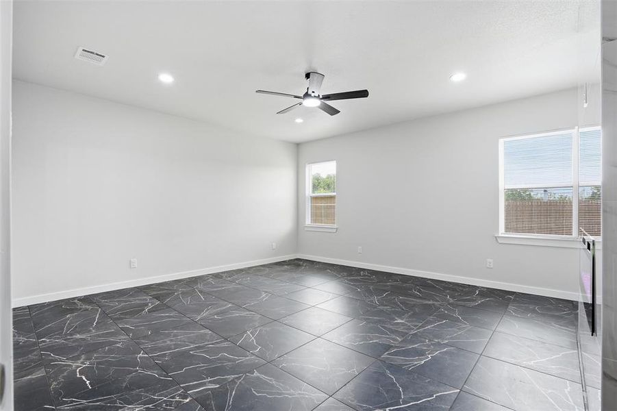 Spacious interior room featuring dark large-format tile flooring with white veining, light-colored walls, and a ceiling fan with integrated lighting