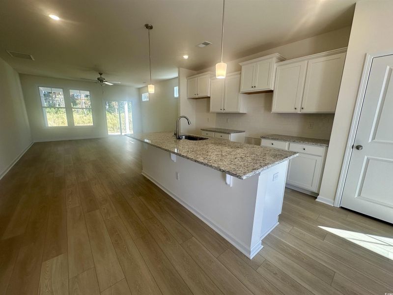 Kitchen featuring granite counters, pendent light fixtures, a kitchen island with sink, ceiling fan, and white cabinetry Kitchen featuring granite counters, pendent light fixtures, a kitchen island with sink, ceiling fan, and white cabinetry
