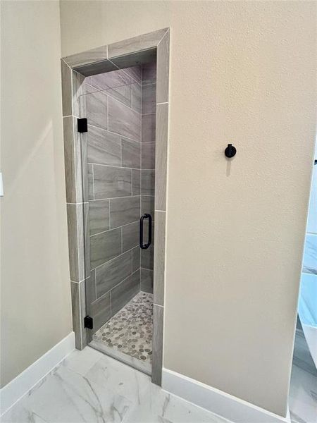Full bath featuring a stall shower and light marble finish floors