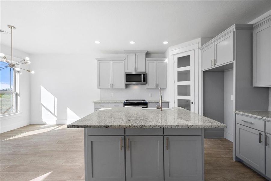 Kitchen featuring appliances with stainless steel finishes, light hardwood / wood-style floors, gray cabinets, a kitchen island with sink, and light stone countertops