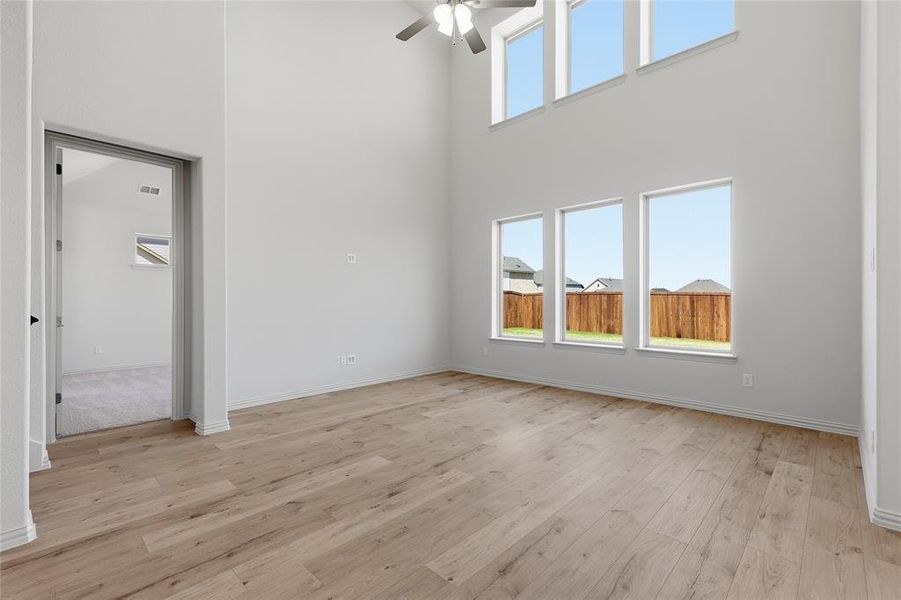 Spacious room featuring soaring ceilings, wood-finish flooring, a contemporary ceiling fan, and multiple windows providing abundant illumination