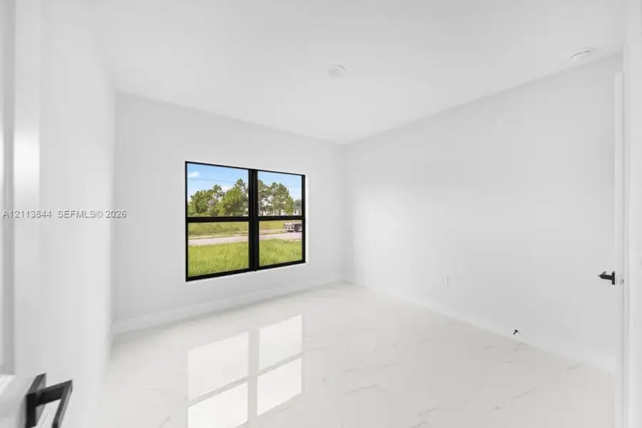 Interior space featuring polished stone-finish tile flooring, neutral wall tones, recessed lighting, and a window with a black frame Interior space featuring polished stone-finish tile flooring, neutral wall tones, recessed lighting, and a window with a black frame