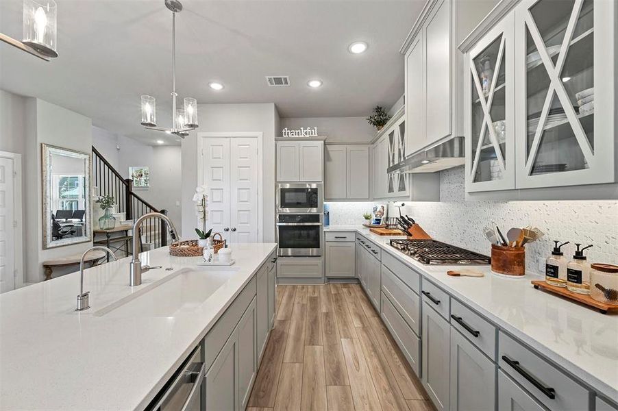 Kitchen with appliances with stainless steel finishes, gray cabinets, tasteful backsplash, light wood finished floors, and under cabinet range hood Kitchen with appliances with stainless steel finishes, gray cabinets, tasteful backsplash, light wood finished floors, and under cabinet range hood