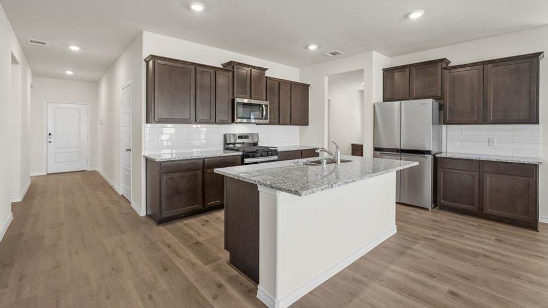 Kitchen featuring dark cabinetry, white subway tile backsplash, stainless steel appliances, and a central island with a granite countertop and sink