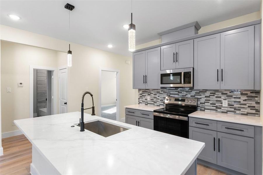 Kitchen with sink, appliances with stainless steel finishes, a kitchen island with sink, light stone counters, and decorative light fixtures