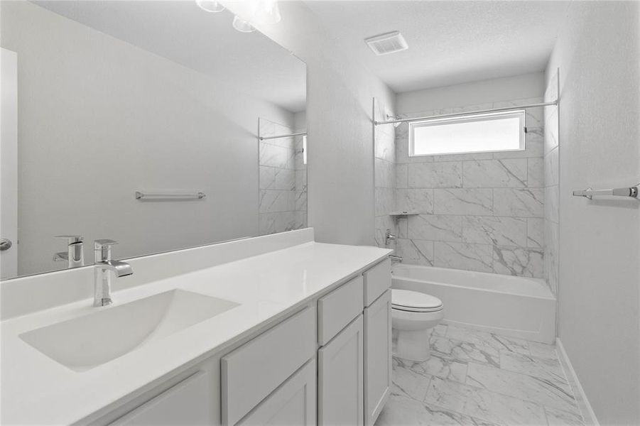 Secondary bath features tile flooring, bath/shower combo with tile surround, white stained wood cabinets, beautiful light countertops, mirror, dark, sleek fixtures and modern finishes.