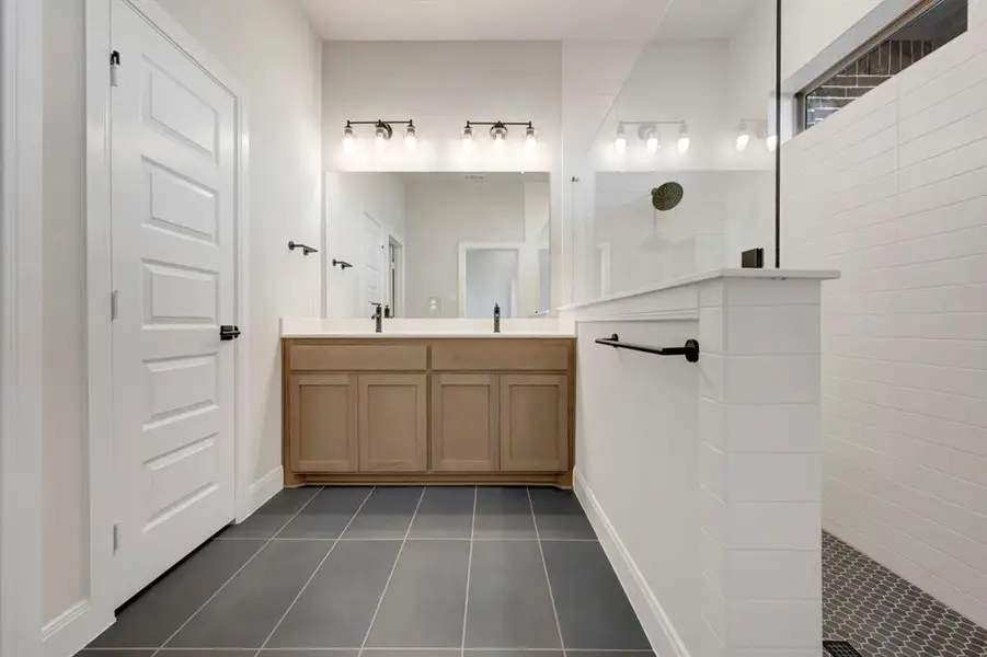 Full bath featuring double vanity, a walk in shower, and dark tile patterned flooring