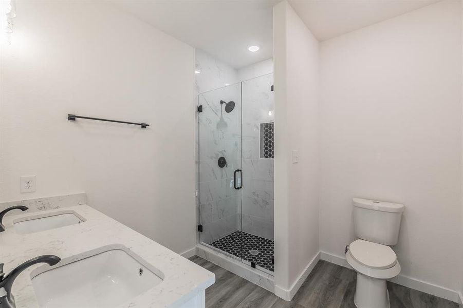 Full bathroom featuring a stall shower, a sink, toilet, and wood finished floors