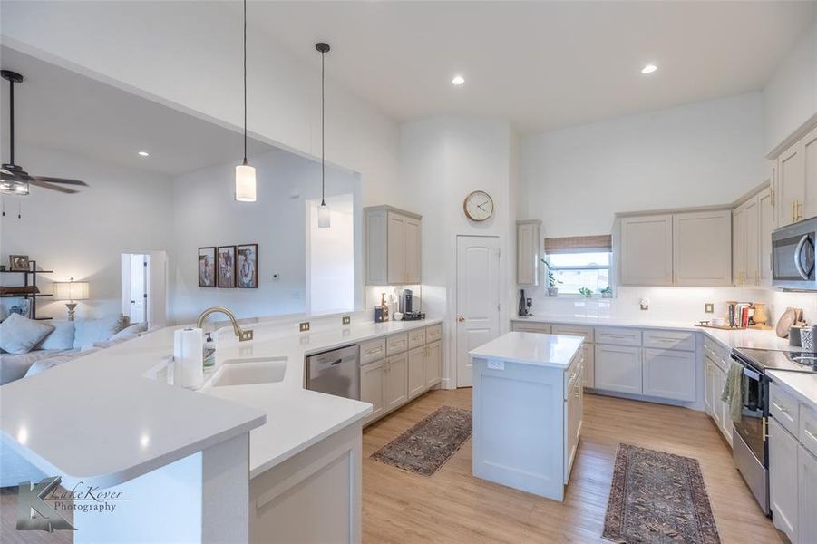 Kitchen with a peninsula, hanging light fixtures, a center island, light wood finished floors, and stainless steel appliances Kitchen with a peninsula, hanging light fixtures, a center island, light wood finished floors, and stainless steel appliances