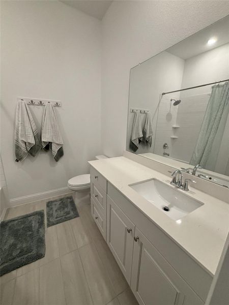 This modern bathroom features a sleek white vanity with ample storage, a large mirror, and a bathtub with a shower. The neutral tile flooring and soft lighting create a clean, inviting space.