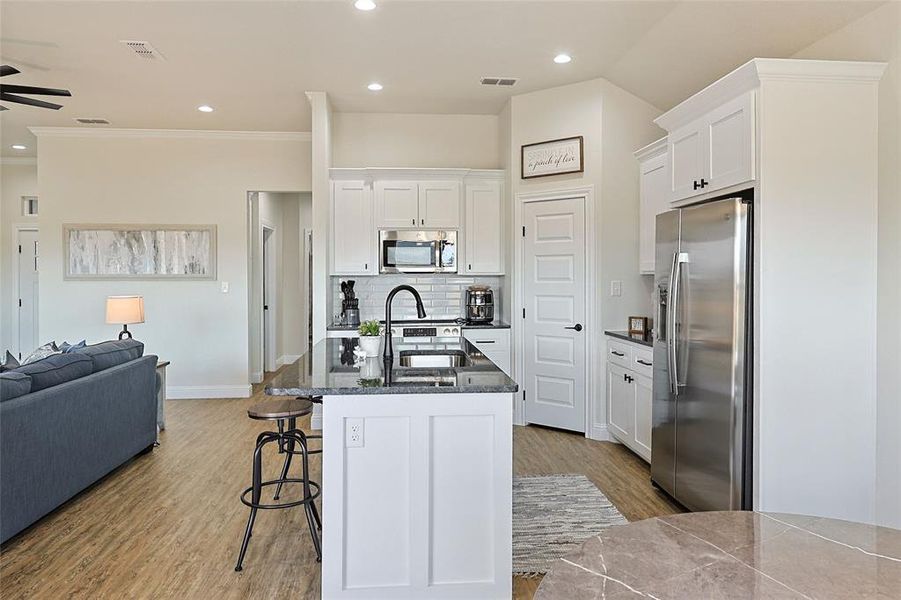Contemporary kitchen featuring white shaker cabinetry, stainless steel appliances, dark granite countertops, a subway tile backsplash, and a central island with an undermount sink