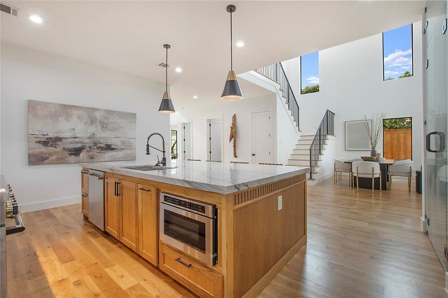 Kitchen with a center island with sink, sink, hanging light fixtures, a healthy amount of sunlight, and light stone counters