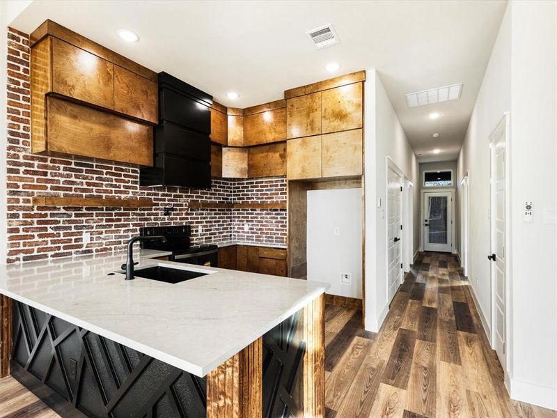 Kitchen with light stone counters, dark wood-style floors, black electric range, a peninsula, and a breakfast bar area