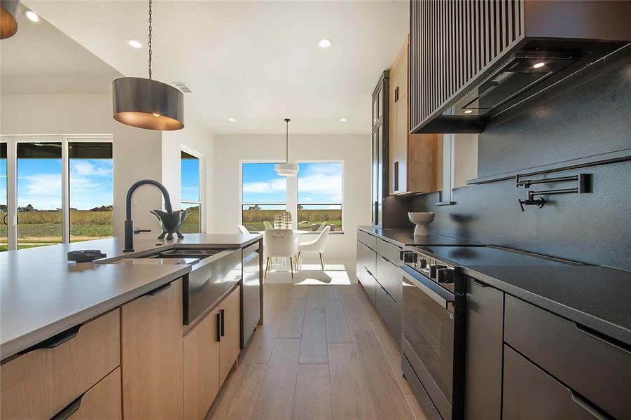 Kitchen with pendant lighting, black electric range oven, wall chimney exhaust hood, modern cabinets, and light wood finished floors Kitchen with pendant lighting, black electric range oven, wall chimney exhaust hood, modern cabinets, and light wood finished floors