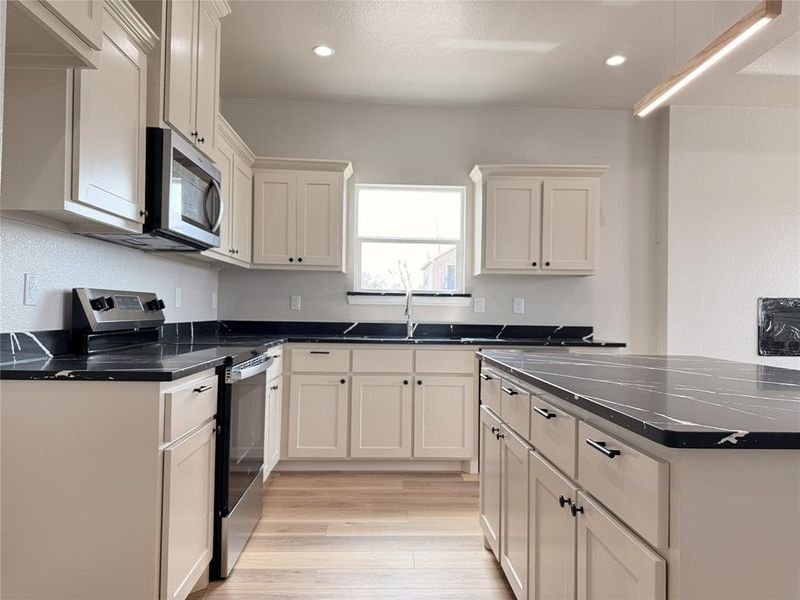 Kitchen featuring stainless steel appliances, light wood finished floors, recessed lighting, dark stone counters, and white cabinetry