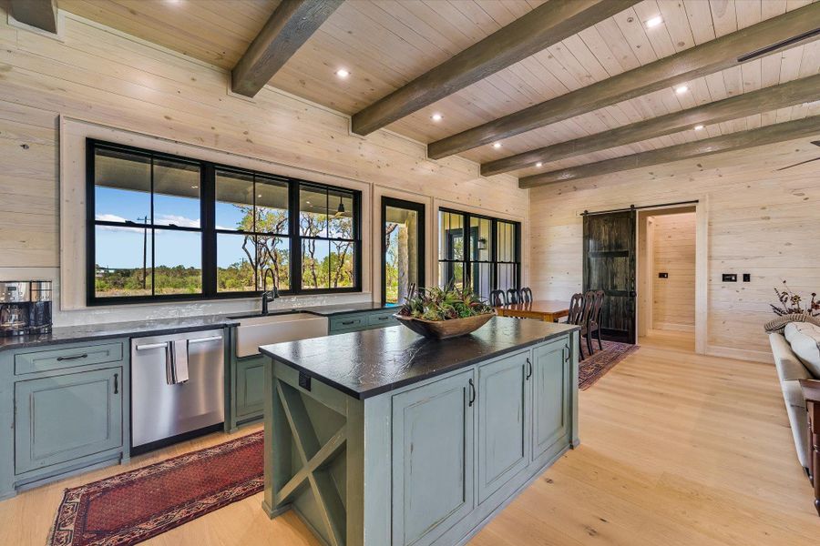 Kitchen with a barn door, a kitchen island, wooden walls, light wood-type flooring, and dishwasher