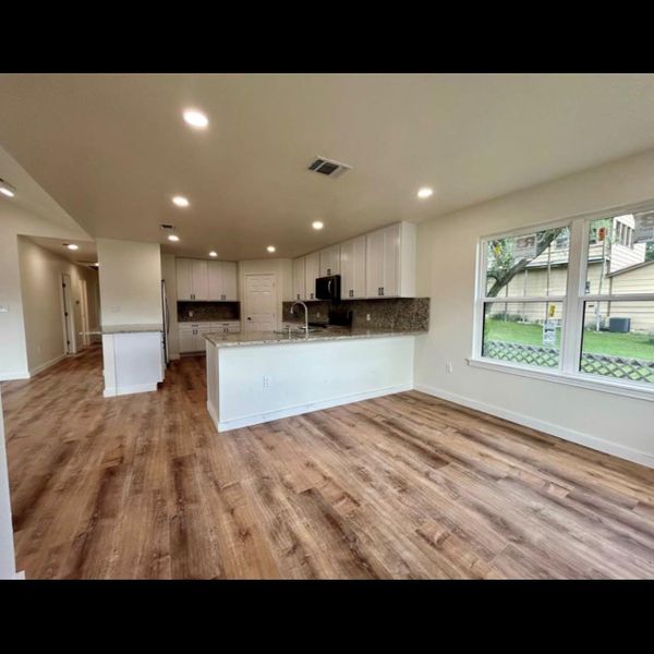 An open-concept kitchen and living area, complete with gleaming granite counters and warm hardwood flooring, await.
