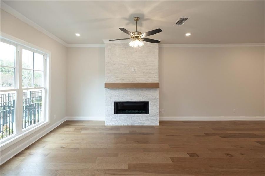 Unfurnished living room with hardwood / wood-style flooring, ornamental molding, ceiling fan, and a fireplace