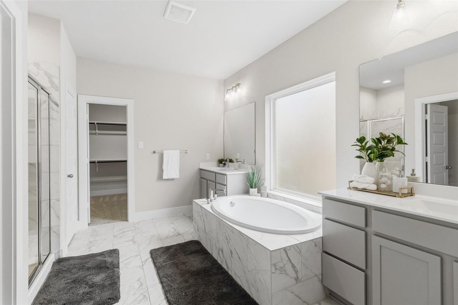 Unwind in your spa-like primary bathroom featuring dual vanities, a soaking tub, separate glass-enclosed shower, elegant tilework, and a large walk-in closet.