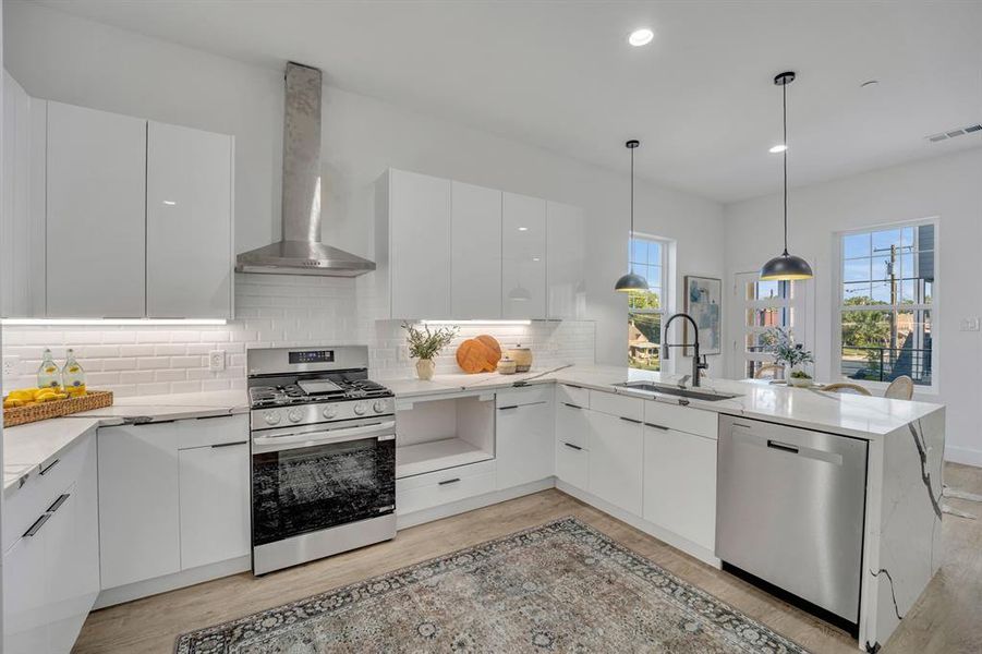 Kitchen with sink, white cabinets, kitchen peninsula, hanging light fixtures, and appliances with stainless steel finishes