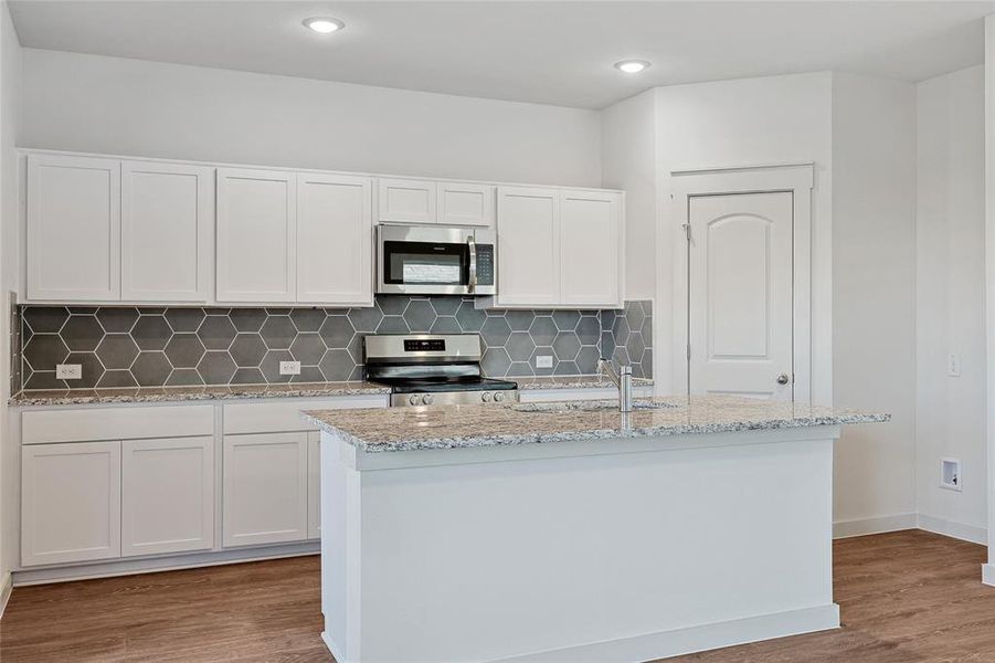 Kitchen with a kitchen island with sink, white cabinetry, stainless steel appliances, and hardwood / wood-style flooring