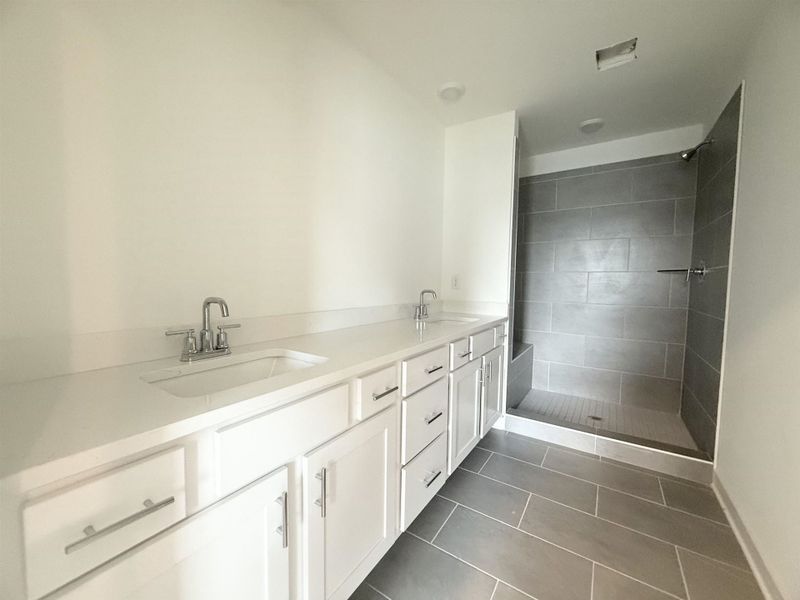Full bathroom featuring double vanity, dark tile patterned floors, and tiled shower
