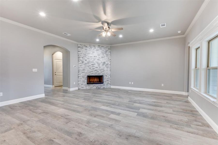 Unfurnished living room featuring ornamental molding, light wood-type flooring, ceiling fan, and a fireplace