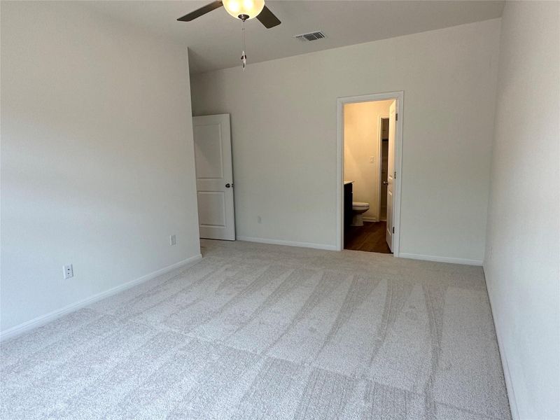 Unfurnished bedroom with light carpet, ceiling fan, and ensuite bathroom