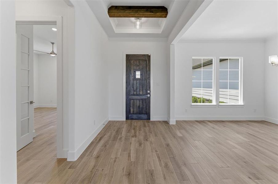 Spacious entry foyer featuring wood-finish flooring, a dark wood-paneled entry door with frosted glass, and a recessed ceiling with a substantial wood beam accent
