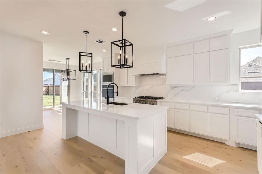 Kitchen featuring sink, a kitchen island with sink, light hardwood / wood-style floors, and tasteful backsplash